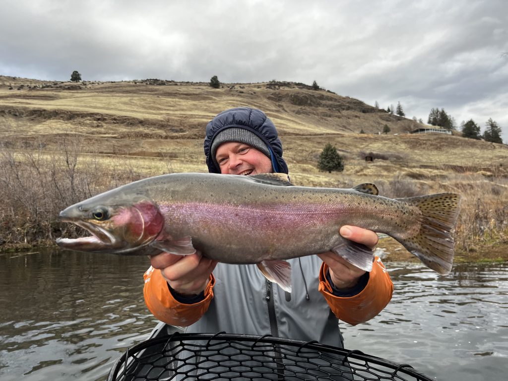 happy angler hoisting a Klamath River Steelhead with the high desert landscape of Hornbrook California in the background